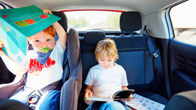 young kids sitting on back seat, reading book while traveling in the car